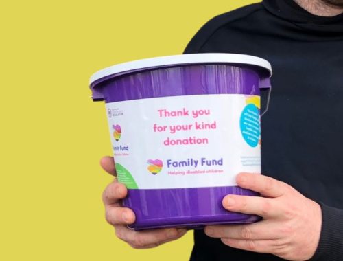 A man in a black hoodie holding a purple Family Fund donation bucket