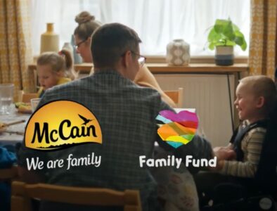 A freezeframe from a McCain Family Fund TV advert with a family sat at a dinner table with a toddler being tickled by his dad