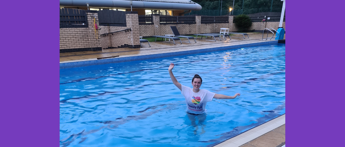 A young woman stands in swimming pool wearing Family Fund t-shirt.