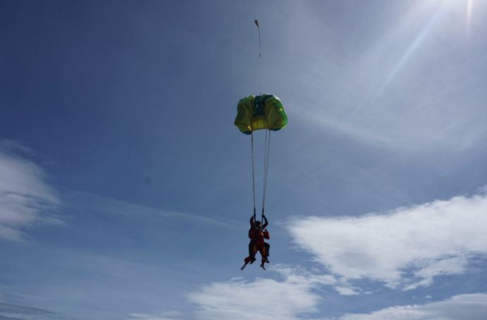 Two people and a parachute opening, silhouetted in the sky