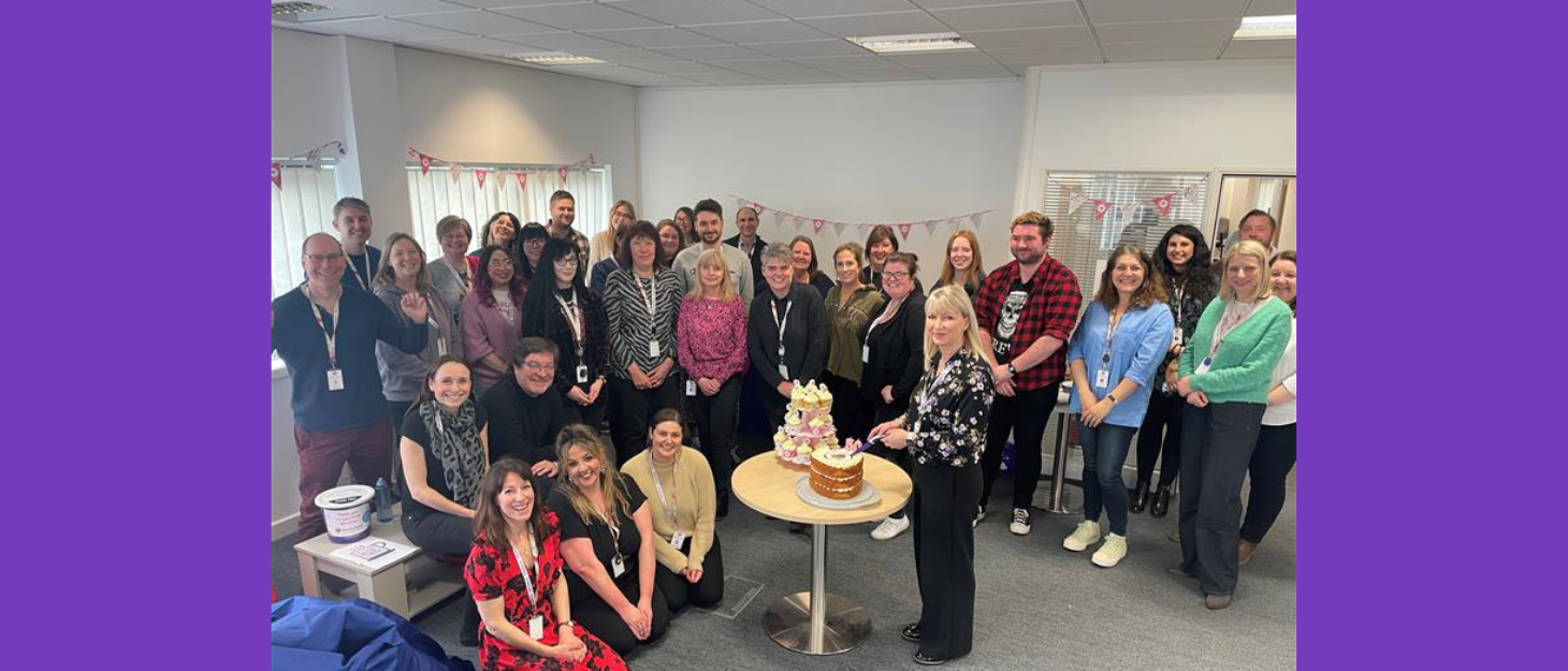 Family Fund team in big group crowded around a 50th Birthday cake in the office