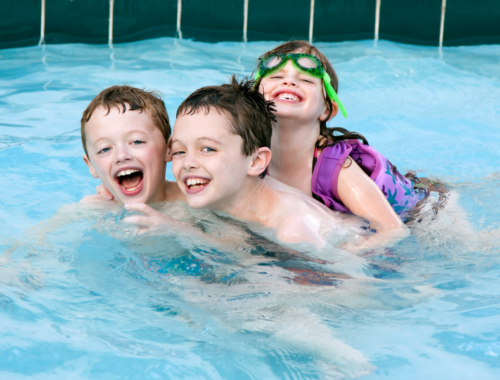 Three children are swimming and playing together in a swimming pool