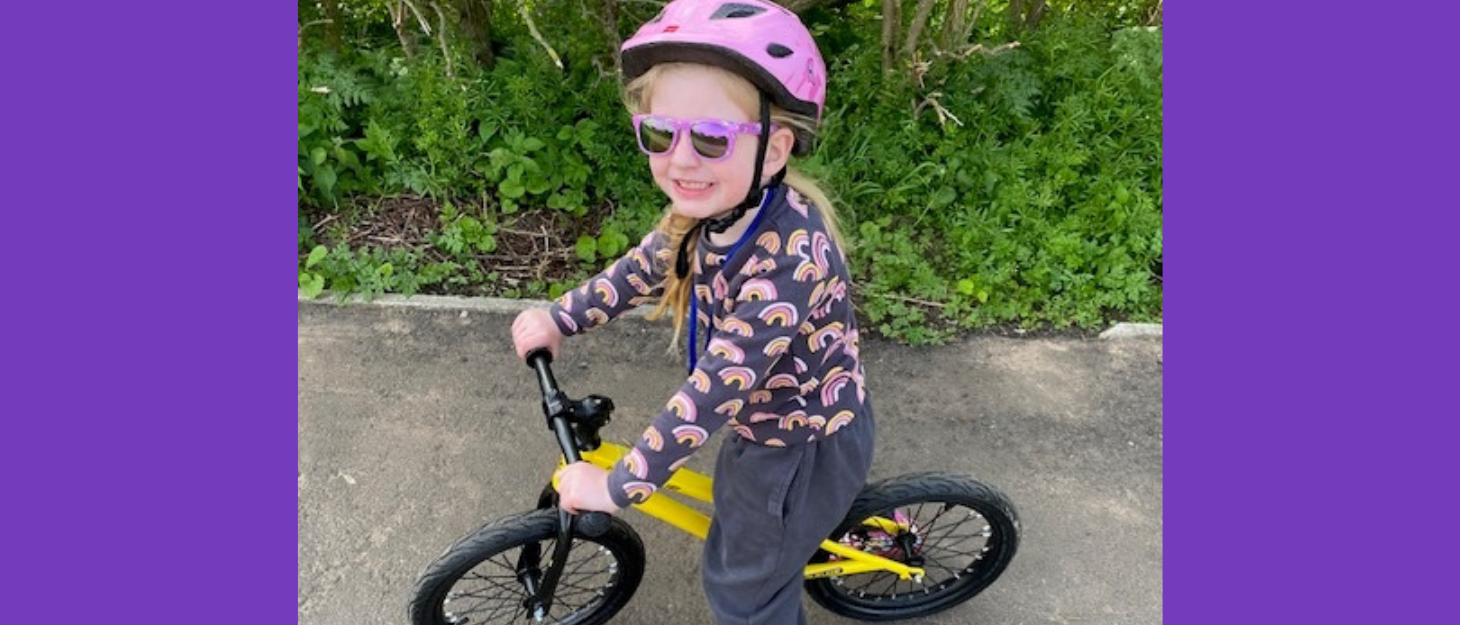 Young girl wearing pink helmet and sunglasses rides her balance bike