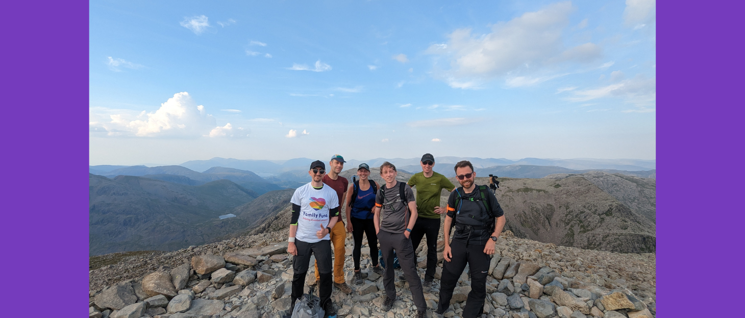 A group of six people on top of a mountain with blue sky and clouds behind them