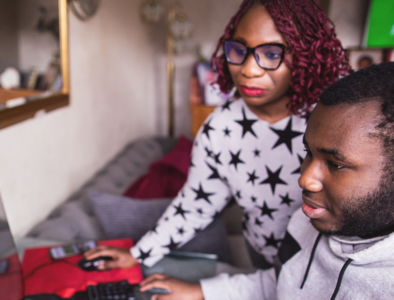 a mum wearing glasses and a starred tee shirt is looking at her computer, with her teenage boy next to her