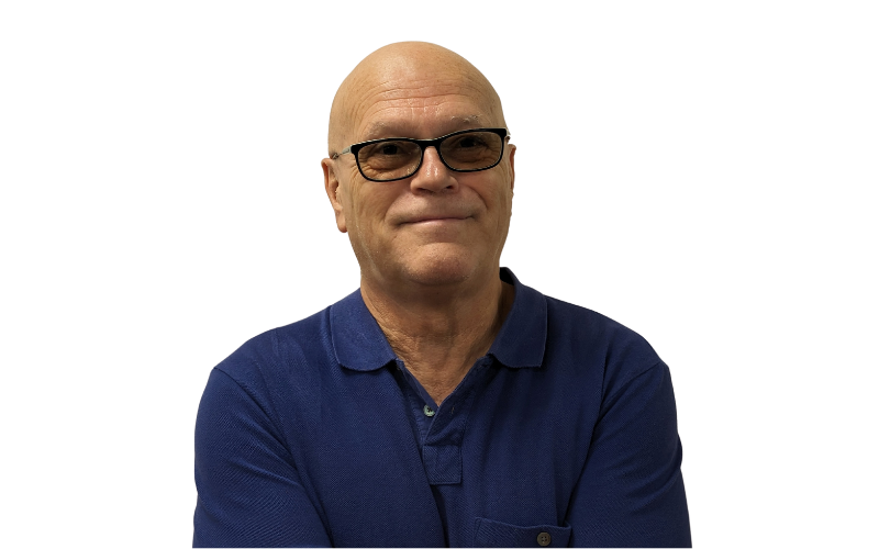 A bald man wearing a blue polo shirt and black glasses is smiling