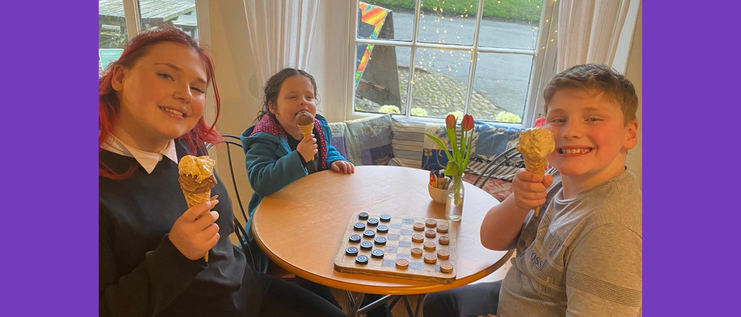 Two sisters and brother sit round a table in a cafe eating ice cream