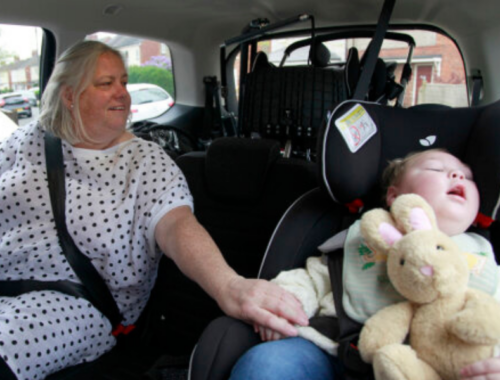 A grandmother and grandson sit together in the back of a car.