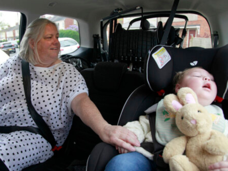 A grandmother and grandson sit together in the back of a car.