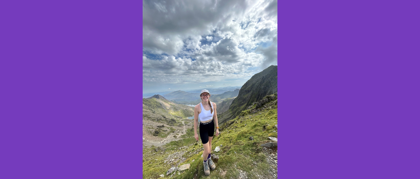 A young woman in shorts and a white vest top, standing in the hills of Snowdon
