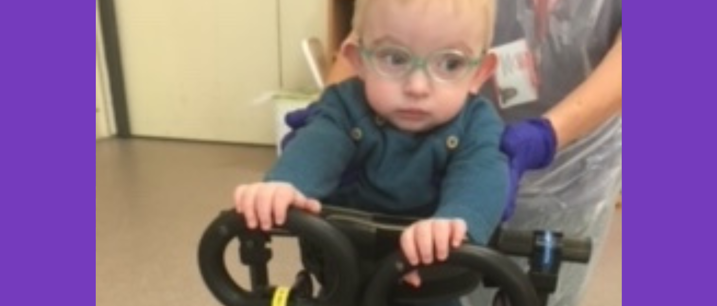 Little boy wearing glasses stands using mobility Fram