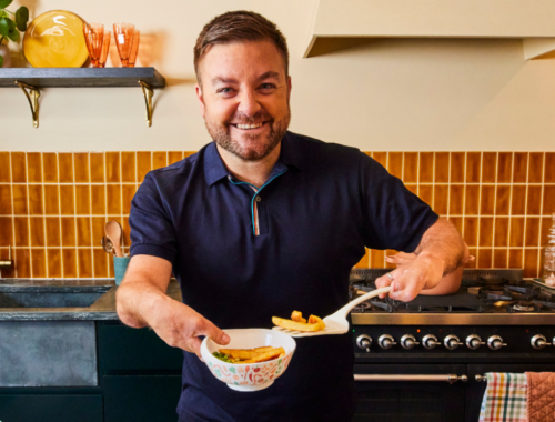 Comedian Alex Brooker stood in a kitchen with the McCain and Family Fund scoop bowl in one hand, and a spatula with chips on in the other